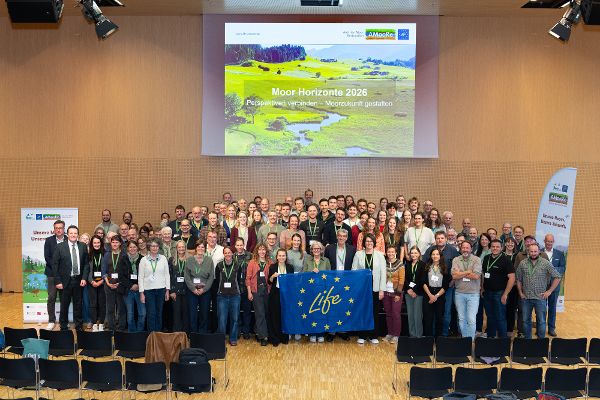 Großes Gruppenfoto von Menschen in einem Saal vor einer Leinwand mit der Aufschrift 'Moor-Horizonte 2026' und einem blauen Banner mit gelben Sternen und dem Schriftzug 'Life'