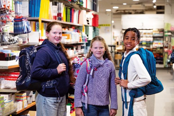 Das Bild zeigt drei Schulkinder mit Rucksäcken in einem Büro- und Papierfachhandel.