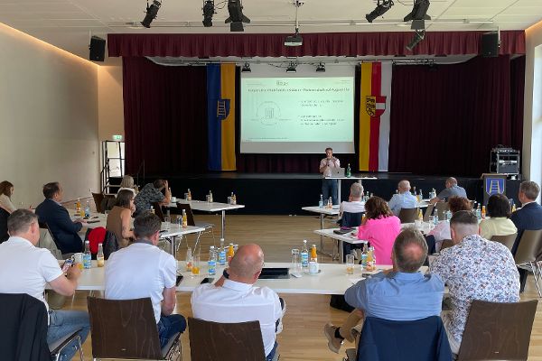 Auf dem Foto ist ein Konferenzraum zu sehen, in dem mehrere Menschen an Tischen sitzen. Sie nehmen an einem Impulstag teil.