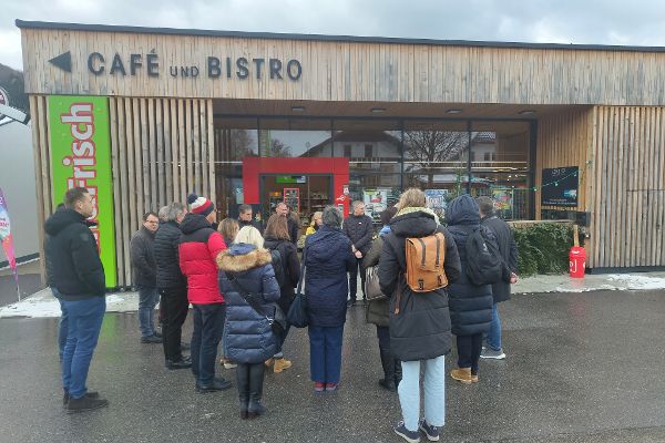 Teilnehmende Personen der Exkursion stehen vor dem Multifunktionshaus Nah und Frisch 