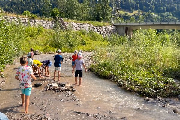 Experimente mit Bauen im Hochwasser: Kinder stellen Häuser im Bachlauf, welcher geflutet wird. 