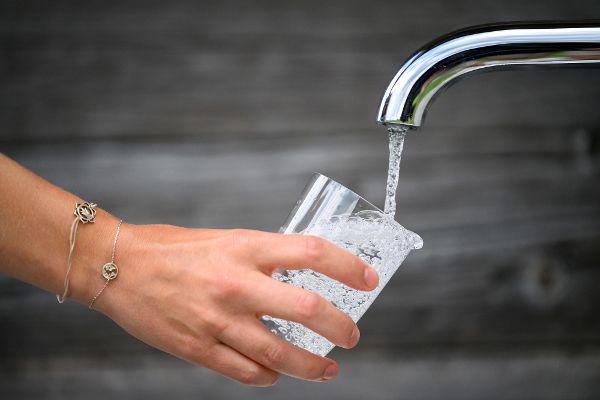 Ein Wasserglas wird unter einem fließenden Wasserhahn aufgefüllt.
