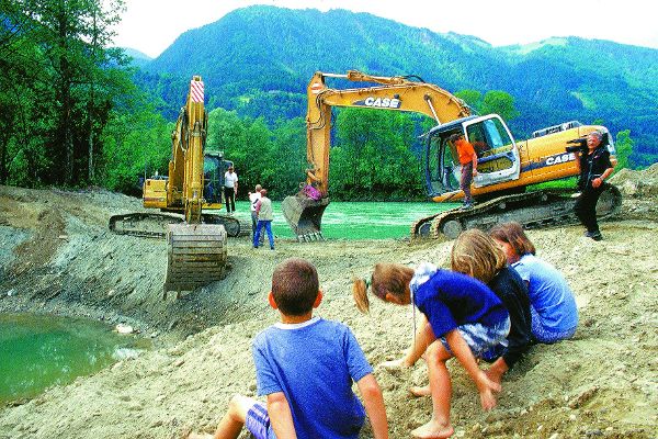 Children are playing on sand hill in the background are excavators