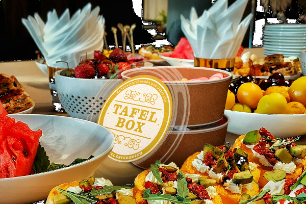 Ein Buffet mit verschiedensten Lebensmitteln, in der Mitte stehen zwei Boxen sowie ein Deckel mit der Aufschrift "Tafel Box"