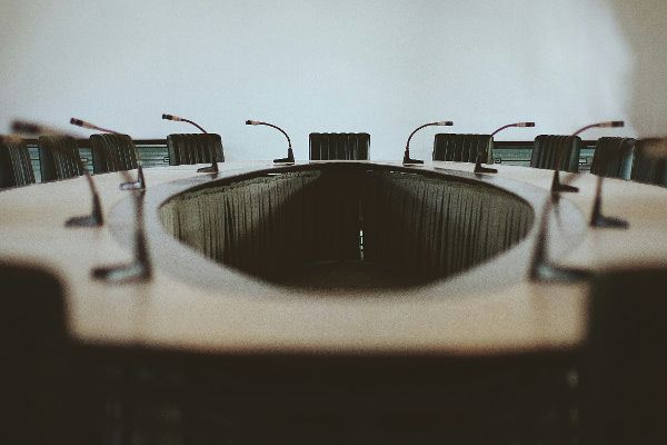 Auf dem Bild ist ein oval förmiger Konferenztisch zu erkennen, mit Stühlen um den Tisch herum gestellt.