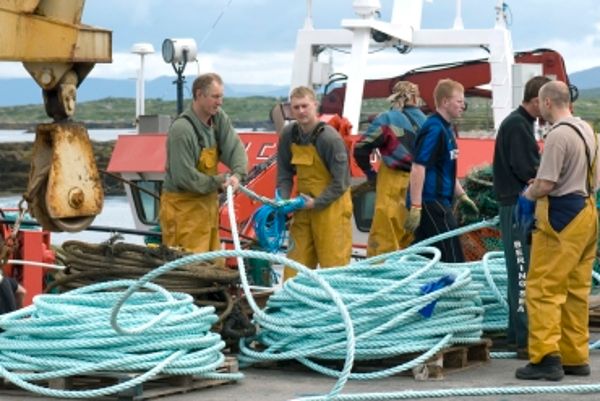 Sieben Fischer auf einem Boot beim Tauaufrollen.