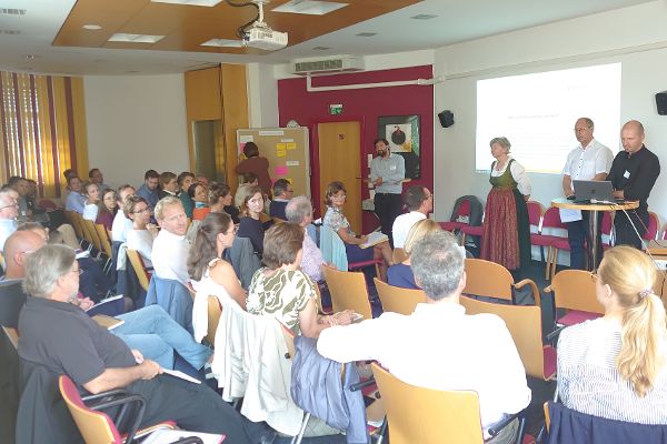Die Teilnehmenden der Veranstaltung stellen Fragen an die Vortragenden Elsa Brunner, Christian Rosenwirth und Elias Molitschnig. Eine Person notiert im Hintergrund an der Pinwand das Gesagte.