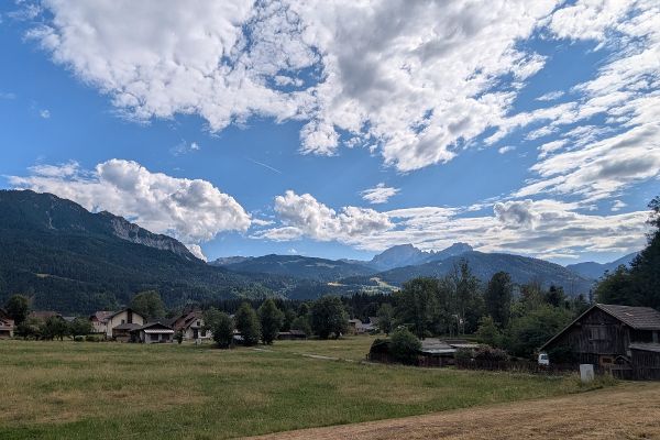 Blick auf eine Landschaft mit blauem Himmel und Bergen im Hintergrund, im Vordergrund ein paar Häuser
