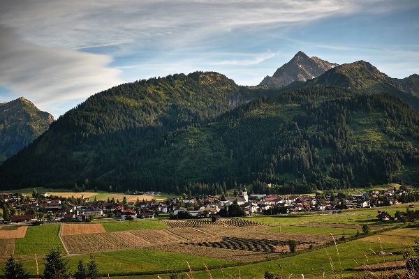 Ländlicher Raum. Im Vordergrund landwirtschaftlich genützte Flächen, dahinter Siedlungsraum und nochmals dahinter die bewaldete Hügellandschaft
