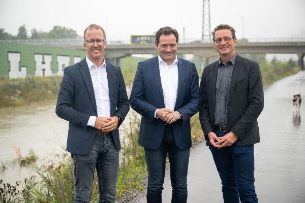 drei in Anzug und weißem Hemd gekleidete Personen, im Hintergrund ein Bachlauf