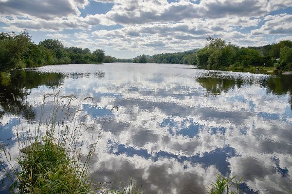 Donau, Wolken dazwischen blauer Himmel umrandet von grünen Bäumen. Die Wolken spiegeln sich im Donauwasser