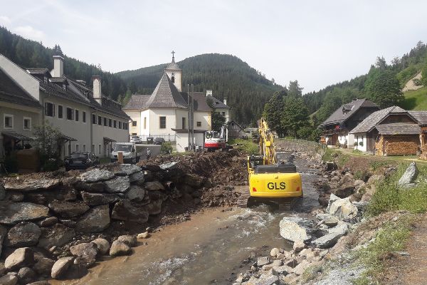gelber Bagger in einem Flussbett, seitlich Flusssteine