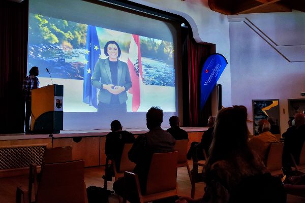 auf einer Wand wird eine Videobotschaft von Bundesministerin Koeistinger abgespielt