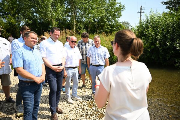 Menschen stehen an einem Kremsufer und hören den Ausführungen einer Mitarbeiterin der Wasserwirtschaft des Landes Oberösterreich zu