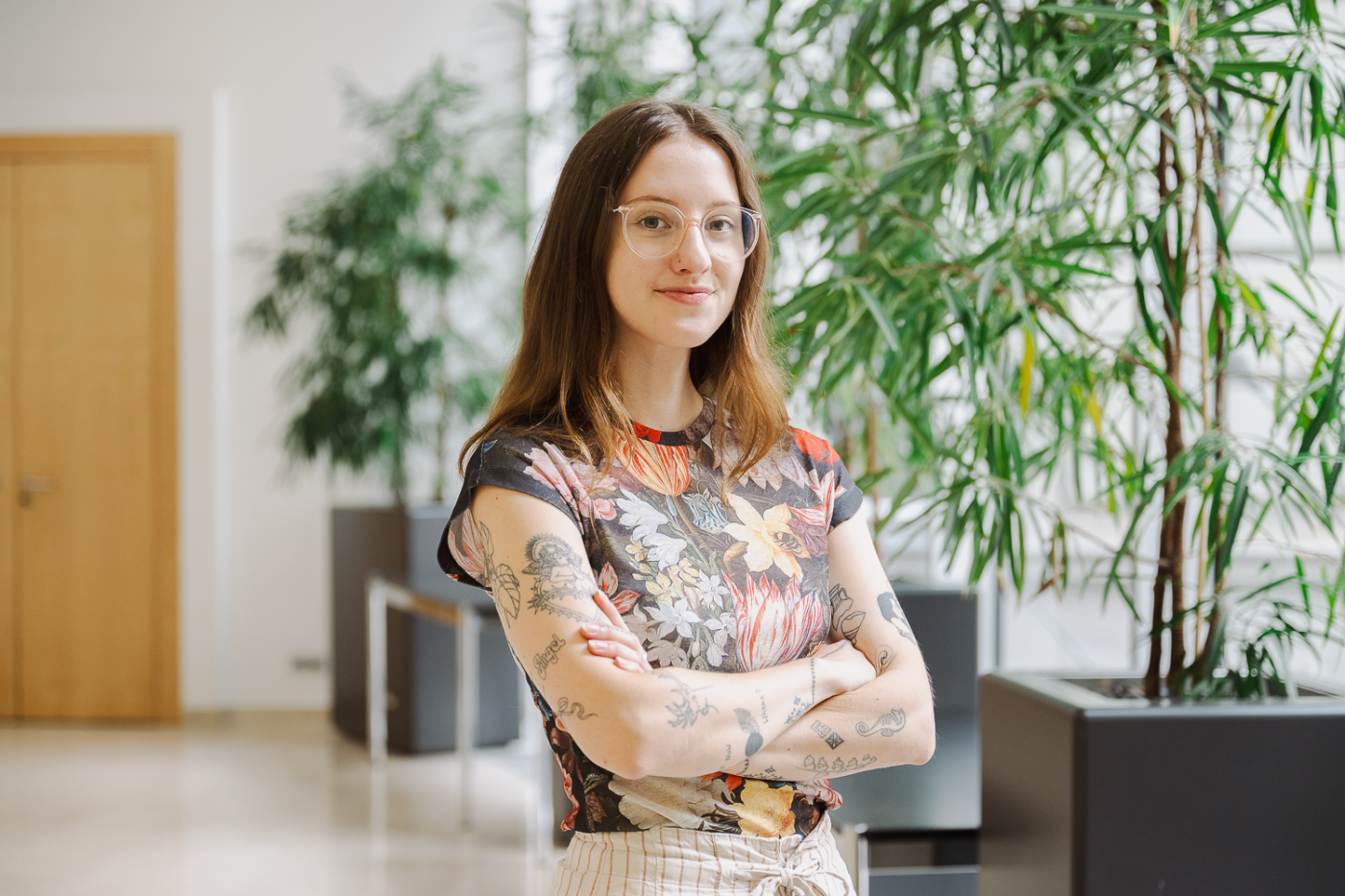 Junge Frau mit buntem T-Shirt und Tattoos lächelt in die Kamera