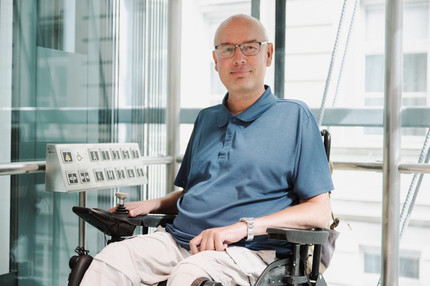 Rollstuhlfahrer im Aufzug lächelt in die Kamera