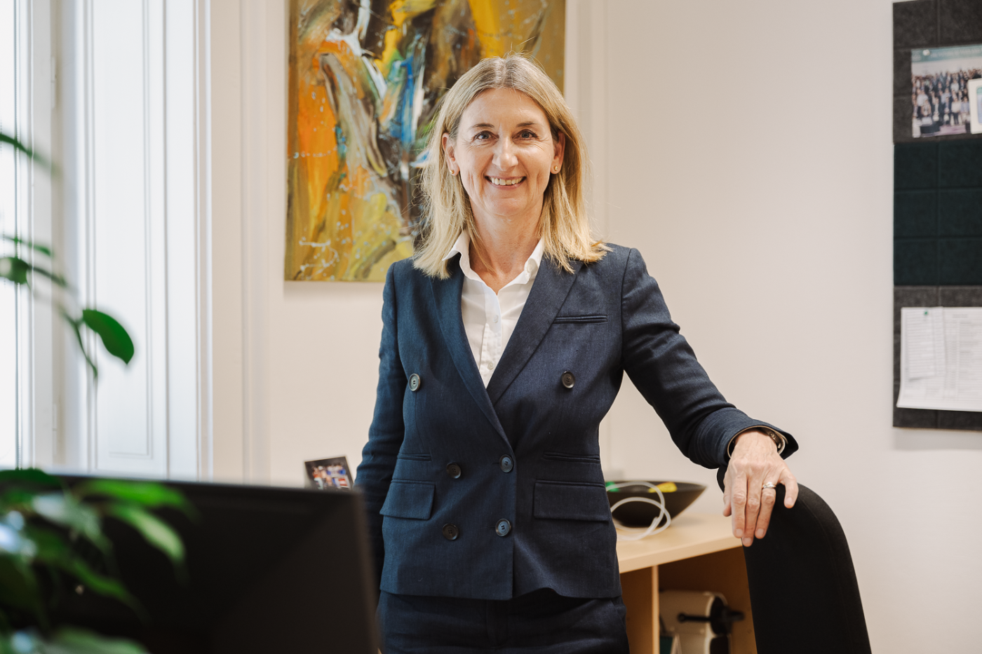 Blonde Dame steht im Büro und lächelt in die Kamera