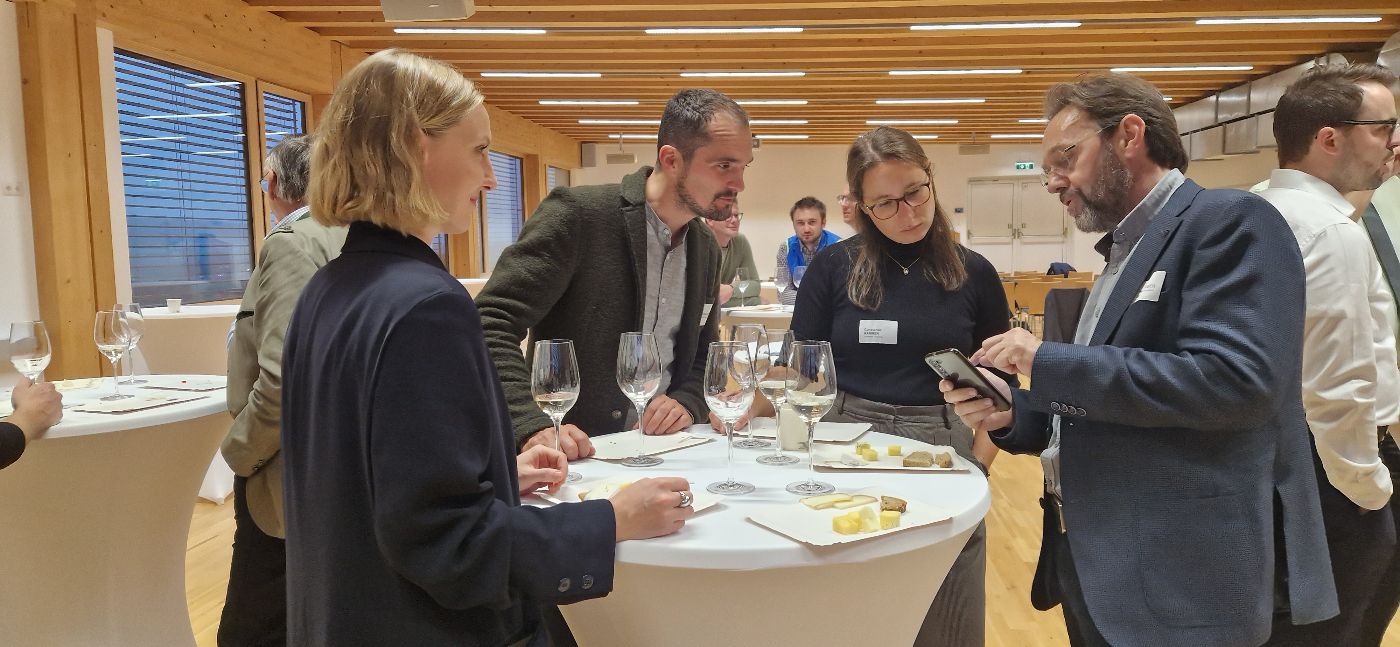 Teilnehmende im Gespräch zum Ausklang der Veranstaltung bei einem Glas Wein rund um einen Stehtisch