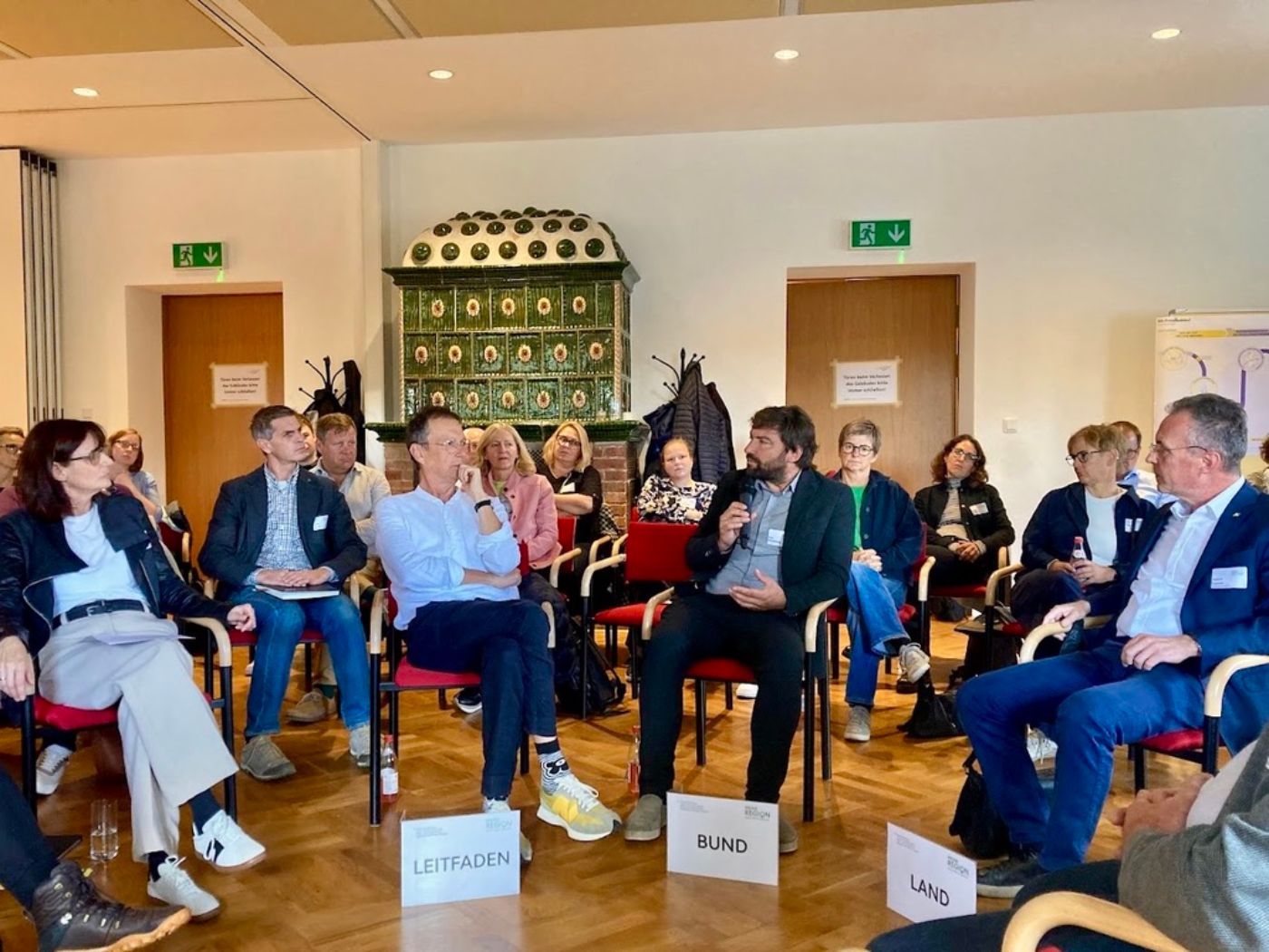 Menschen sitzen im Sesselkreis und diskutieren den vorangegangenen Vortrag. 