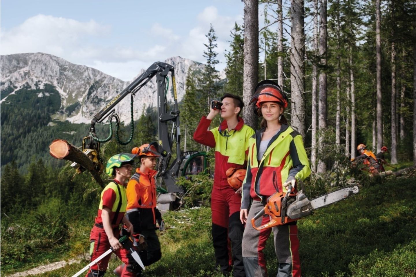 Schülergruppe in Holzfällerausrüstung auf einem Hang und im Hintergrund ein Wald