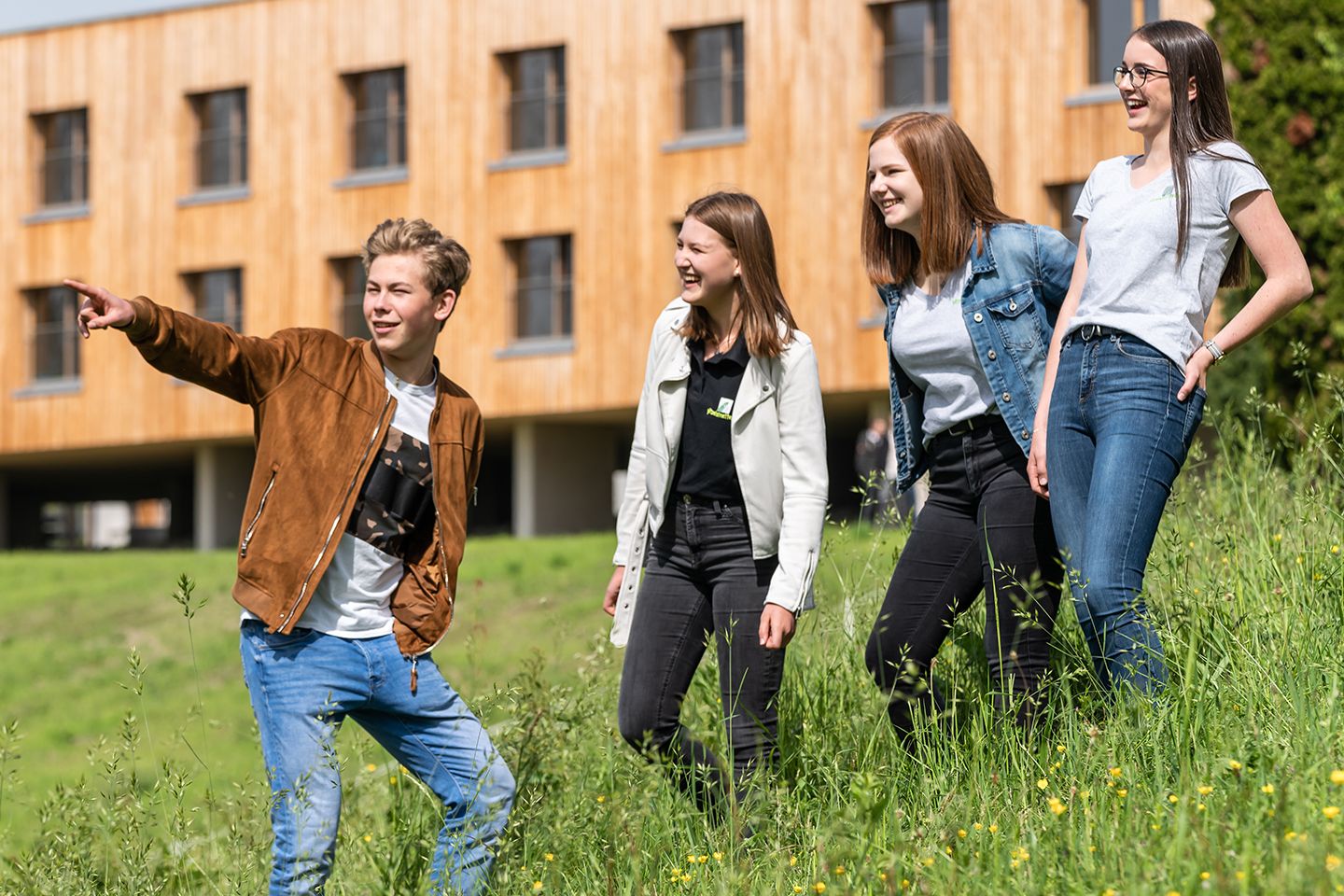 Ein Bursch und drei Mädchen, die auf einer Wiese vor dem Schulgebäude stehen