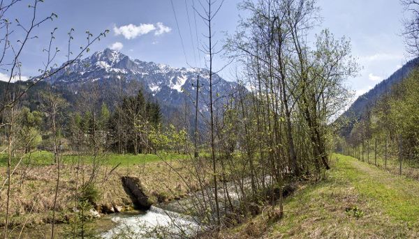 In der Mitte fließt ein Bach. Links und rechts das Bachufer und Hecken. Im Vordergrund ein beschneiter Berg.