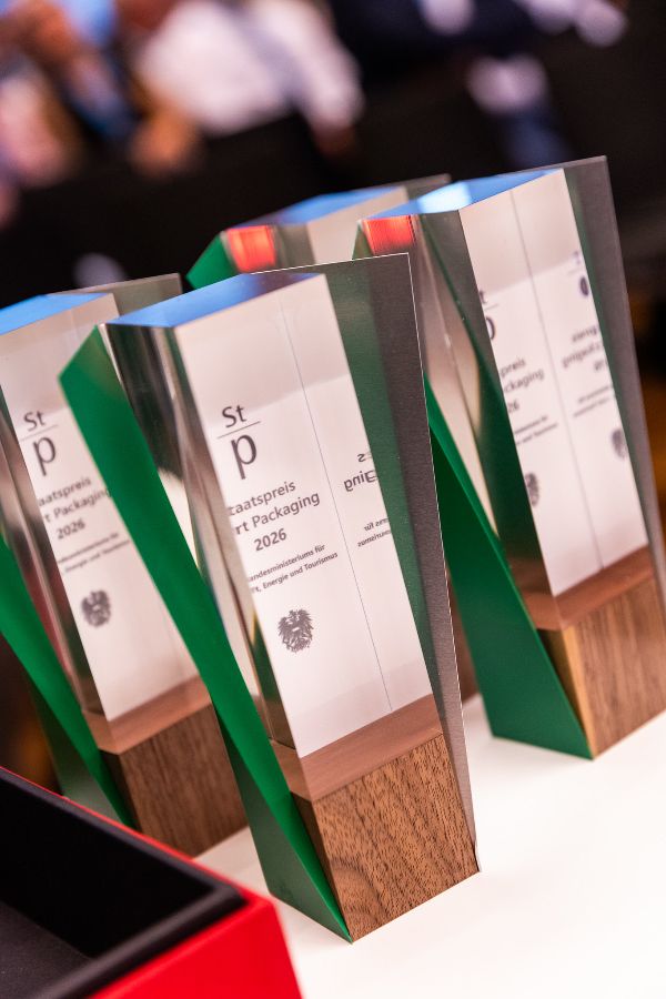 Mehrere moderne Trophäen mit Holzsockel und spiegelnder Oberfläche, darauf Text zu einem Verpackungspreis 2026