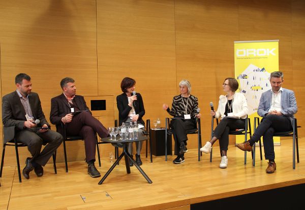 Podiumsdiskussion mit 6 Personen auf Sesseln auf einer Bühne