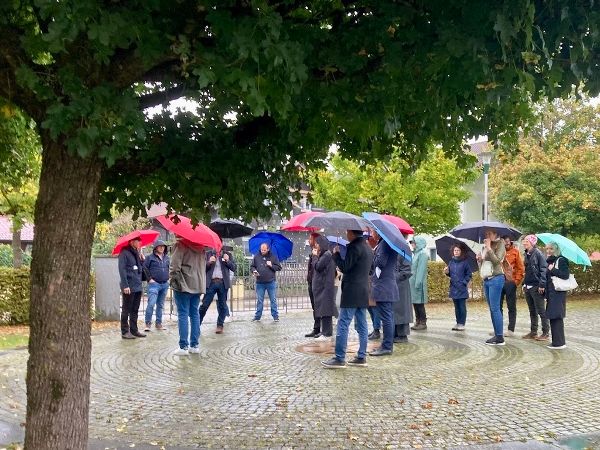 An der Exkursion teilnehmende Menschen mit Regenschirmen stehen auf dem Friedhofsplatz