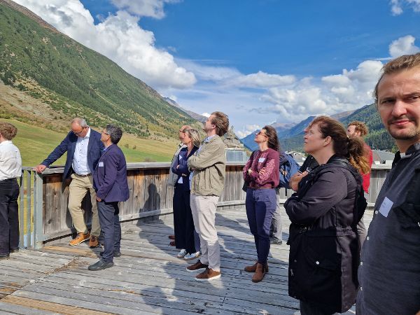 Gruppe von Menschen steht auf einer Holzterrasse vor Berglandschaft und blickt nach oben