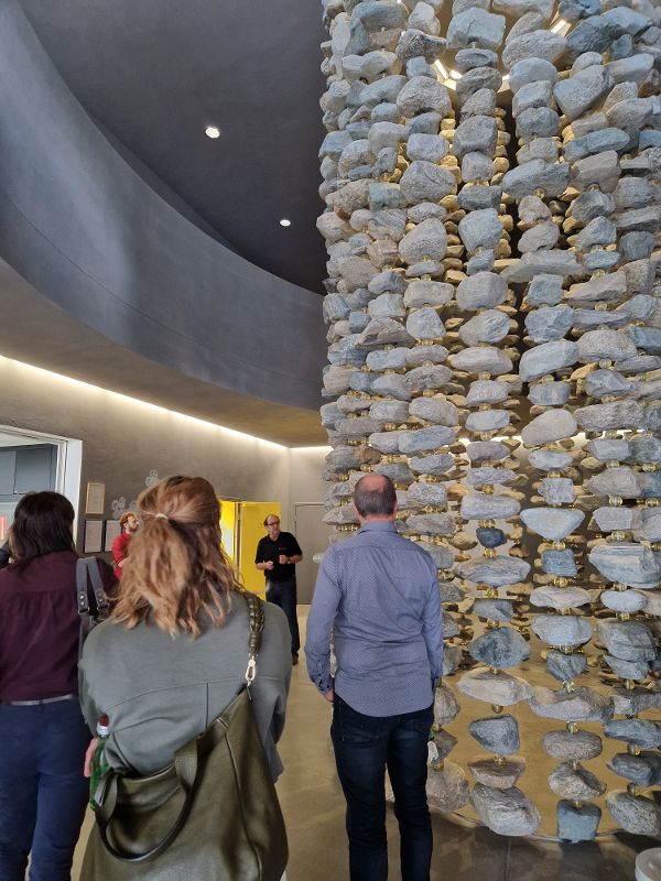 Mehrere Personen stehen vor einer hohen, runden Steinskulptur in einem modernen Innenraum mit abgerundeter Decke und indirekter Beleuchtung