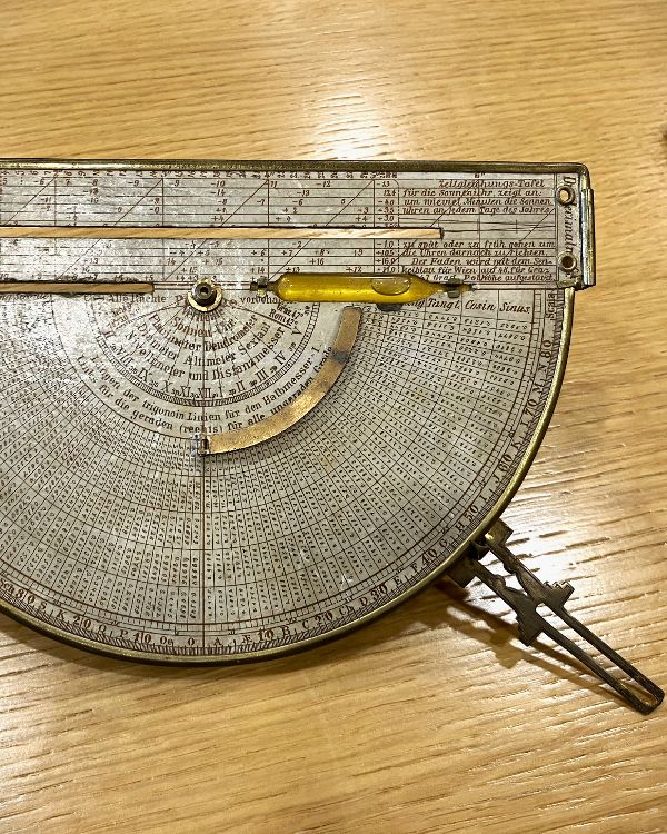 Ein historisches Messgerät bzw. eine handliche Sonnenuhr liegt auf dem Tisch.