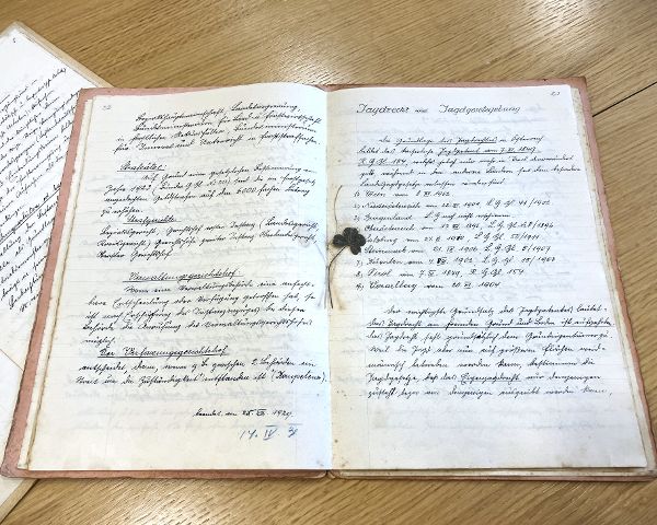 Das handgeschriebene Forst- und Jagdgesetz in einem historischen Buch. Als Lesezeichen liegt ein echtes vierblättriges Kleeblatt in der Buchmitte.
