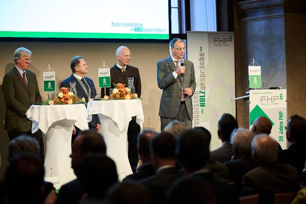 FHP-Vorsitz Erich Wiesner mit Mikro auf der Bühne, im Hintergrund die drei vorangegangenen Vorsitzenden