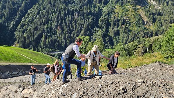 Bundesminister Norbert Totschnig mit Stipendiat:innen beim Überqueren einer Baustelle der Wildbach- und Lawinenverbauung 