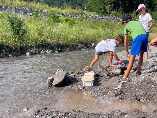 Experimente mit Bauen im Hochwasser: Kinder stellen Häuser im Bachlauf, welcher geflutet wird. 