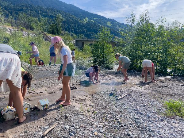 Experimente mit Bauen im Hochwasser: Kinder stellen Häuser im Bachlauf, welcher geflutet wird. 