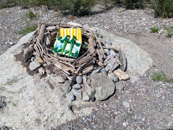 Gebasteltes Haus mit Hochwasser-Schutzmaßnahmen aus Ästen und Steinen auf einer Anhöhe. 
