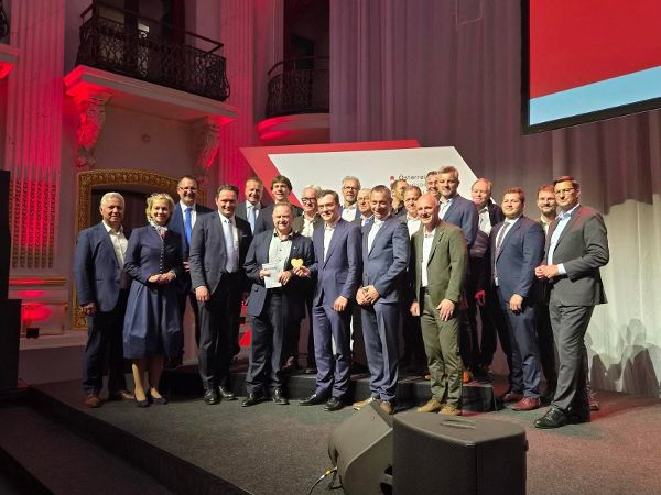 Eine große Gruppe von Personen posiert vor dem Logo des Staatspreis Holzbau