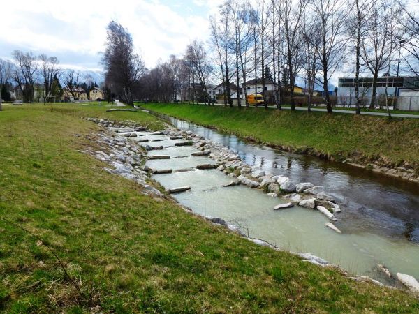 Das Bild zeigt ein mit Steinen struktieriertes Gewässer in mitten einer Wiesenlandschaft