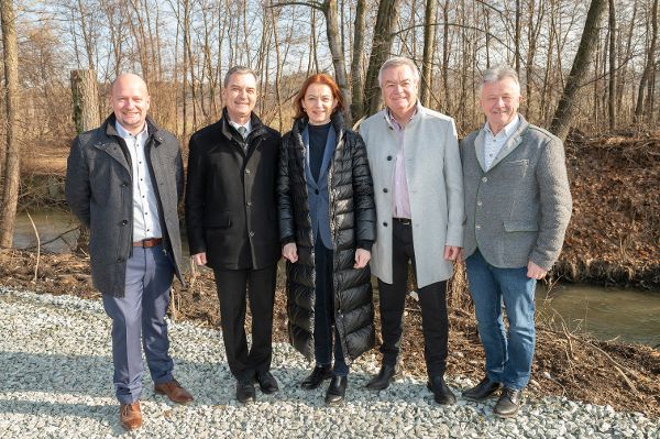 jeweils zwei Herren stehen rechts und links, in der Mitte eine Dame, vor einem Fluss