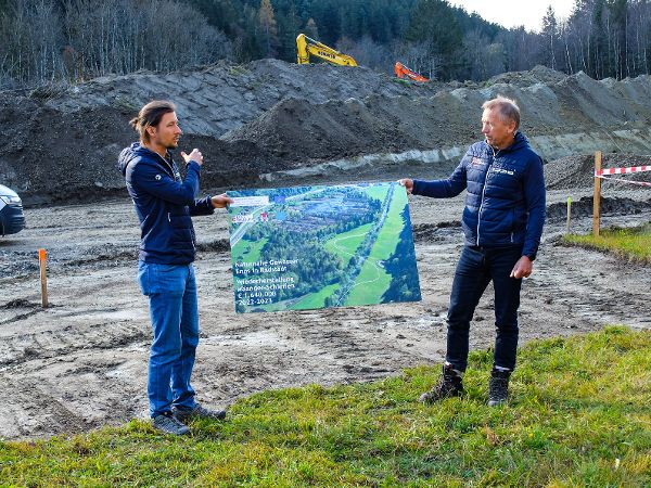 zwei Personen halten ein Flusslandschaftsfoto, im Hintergrund Baustellenbeginn
