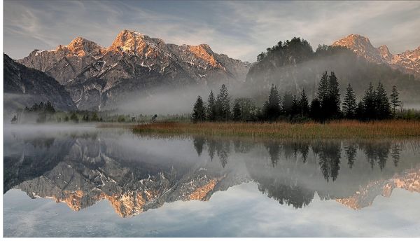 Auf dem Bild ist ein Almsee zu sehen in dem sich Berge und Bäume spiegeln