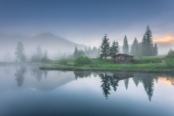 Auf dem Bild ist ein See zu sehen in dem sich die umliegenden Bäume und Berge spiegeln