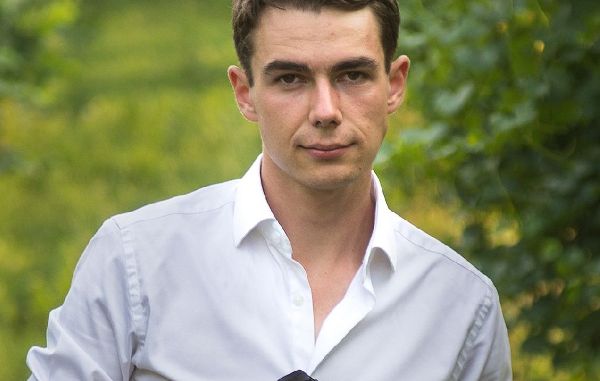 Paul Breuss steht mit seinem Fotoapparat in der Hand in einem Weingarten