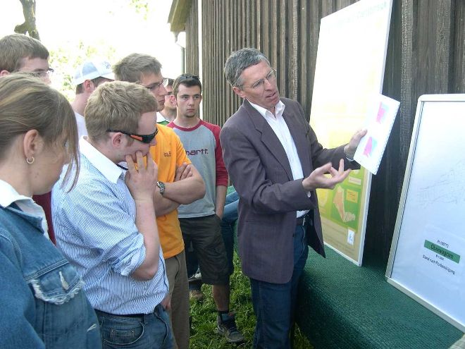 Besprechung vor eine Tafel im Freien, an der Rückseite eines Stadels