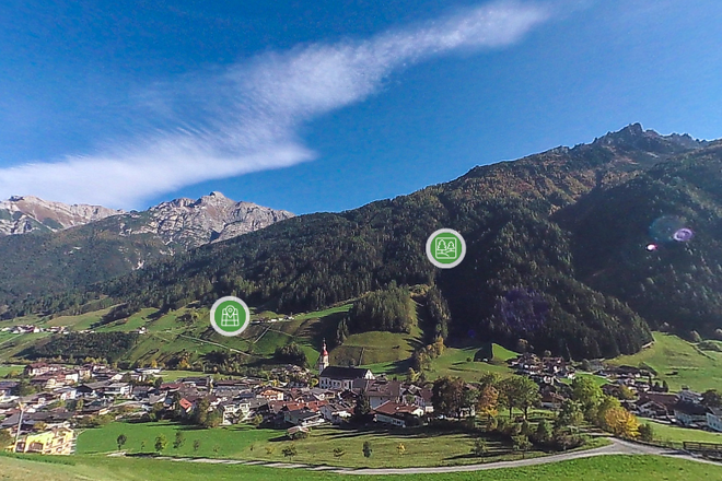 Hügel über einem Dorf im Tal, darauf grüne Info-Punkte