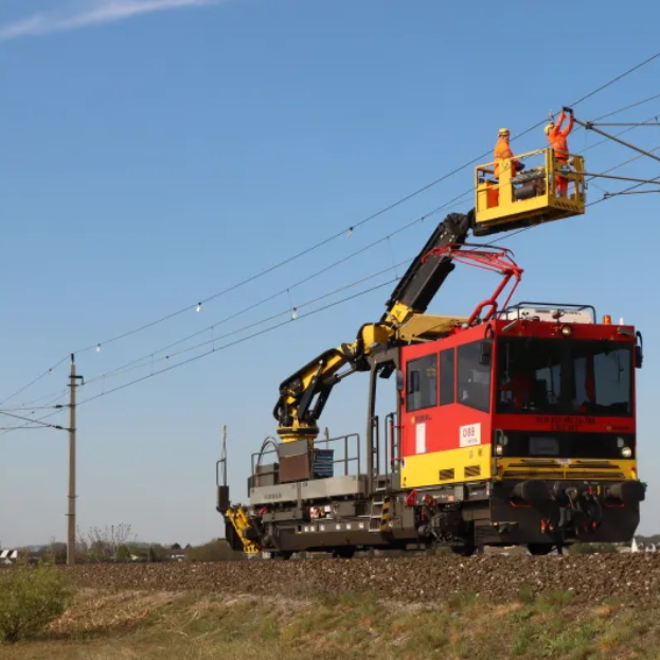 Arbeitszug mit Hebebühne und zwei Arbeitern in orangener Schutzkleidung über Gleisen unter blauem Himmel