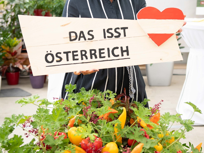 Holzschild mit einer Österreich-Flagge in Herzform und dem Text: Das isst Österreich, darunter regionales Gemüse