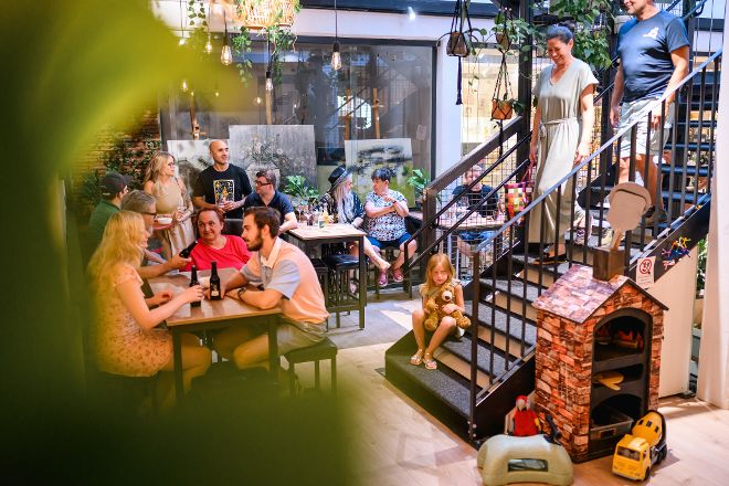 Zu sehen ist der Marktplatz des Kleinstadtbiotops. Kinder spielen und Menschen sitzen am Tisch zusammen. 